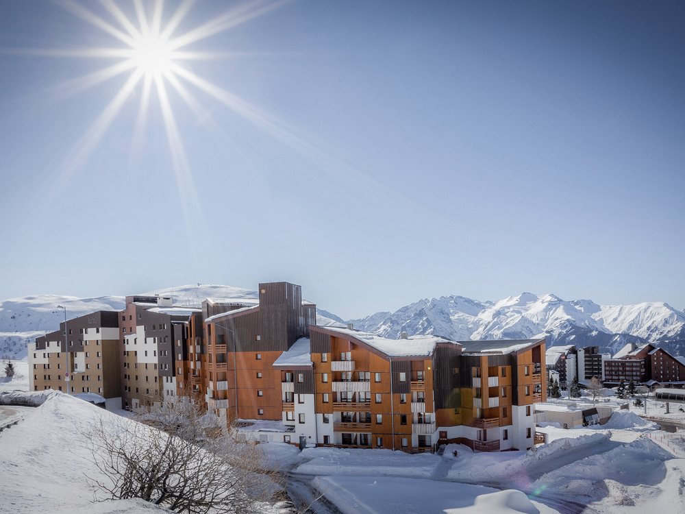 Le Village Club MMV Les Bergers sous la neige et le soleil, ses bâtiments de bois face aux sommets