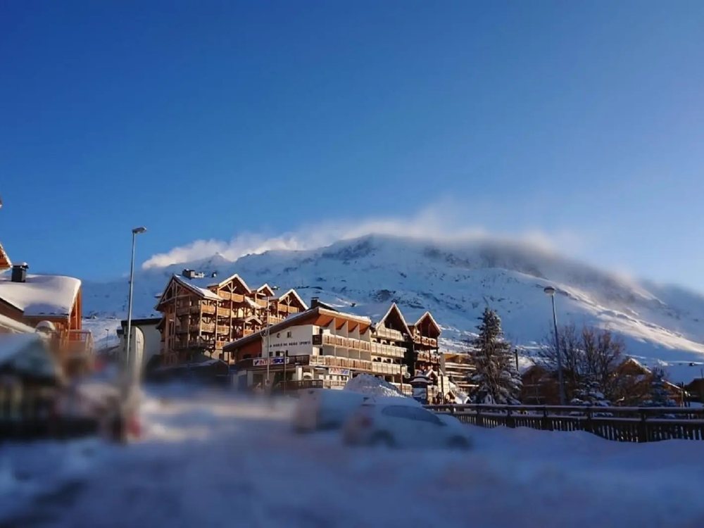 Les chalets de l'Alpe d'Huez sous la neige autour des Bruyères, la montagne et un ciel bleu en fond