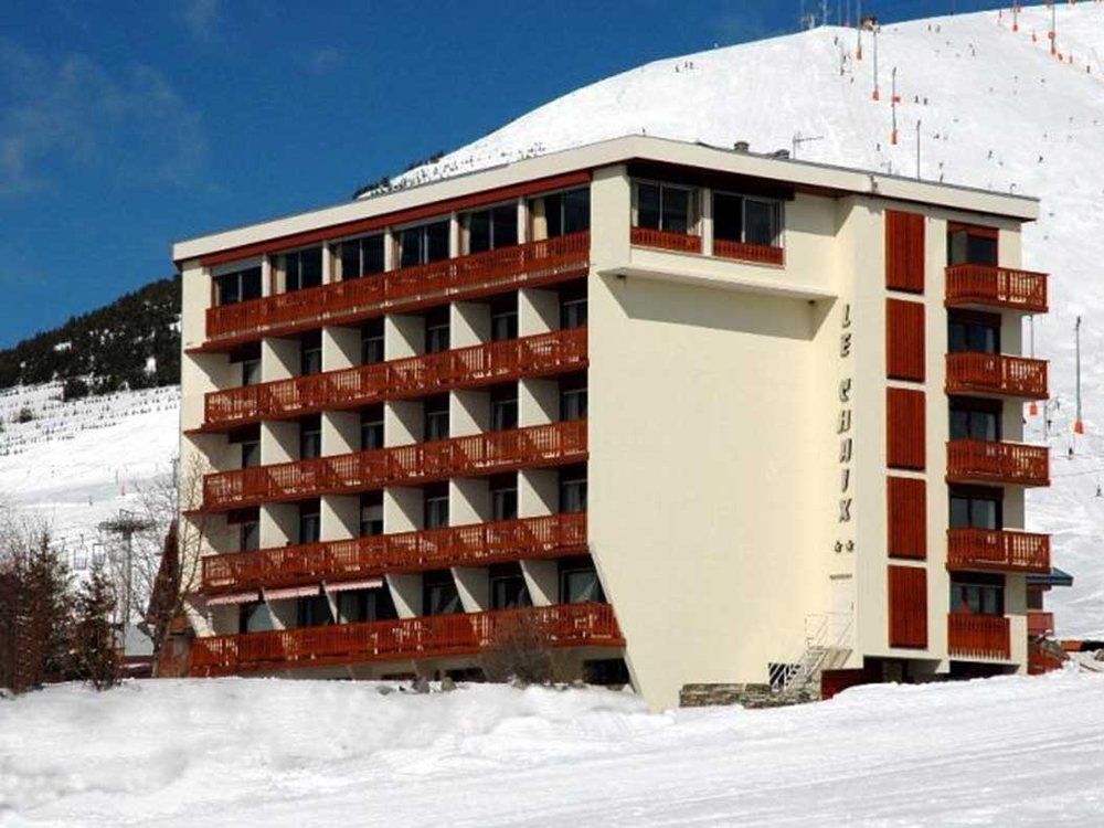 L'Hôtel Eliova Le Chaix sous la neige, sa façade aux balcons rouges et son enseigne, face aux pistes