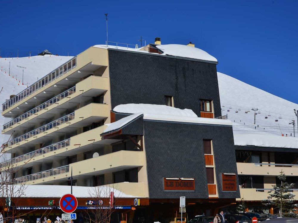 L'Hôtel Le Dôme sous la neige, sa façade aux balcons et ses loggias face aux pistes, ciel bleu