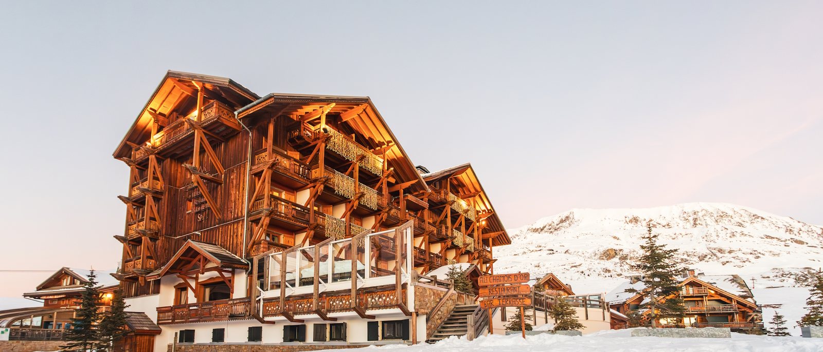 L'Hôtel Au Chamois d'Or sous la neige à l'Alpe d'Huez, ses chalets de bois aux balcons ouvragés et la montagne enneigée en fond