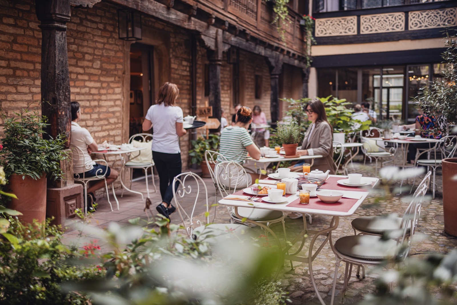 La cour pavée de l'hôtel Cour du Corbeau à Strasbourg, poteaux de bois sculptés, coursives et tables du petit-déjeuner