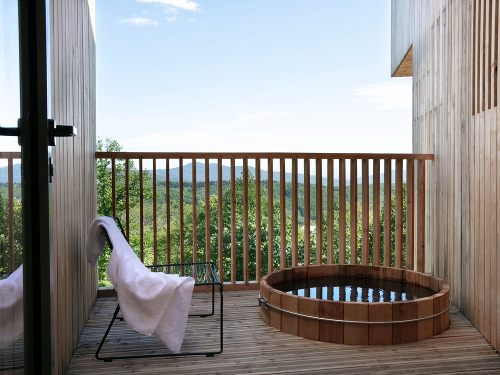 La terrasse en bois d'une hytte Fjell au 48° Nord, son bain nordique en bois, une chaise longue et la vallée des Vosges