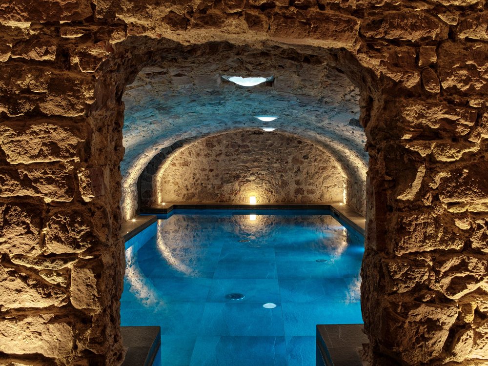 La piscine intérieure de 5 Terres vue à travers une arche de grès, sous une voûte de pierre éclairée