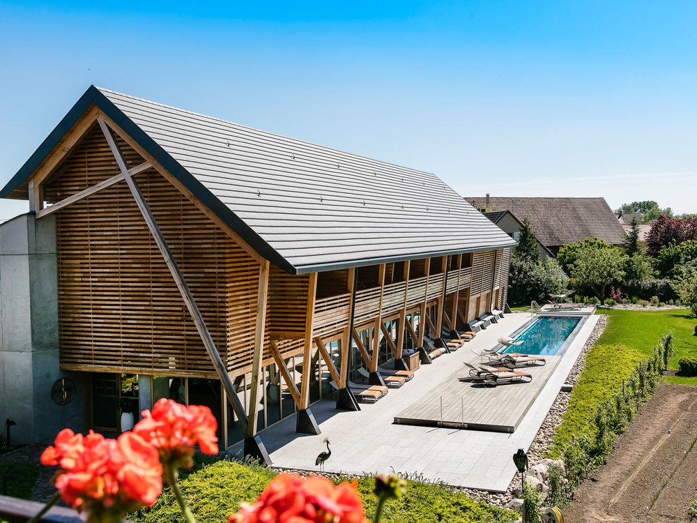 La grange contemporaine du Spa des Saules à l'Hôtel des Berges, sa longue piscine extérieure et ses transats, des géraniums au premier plan