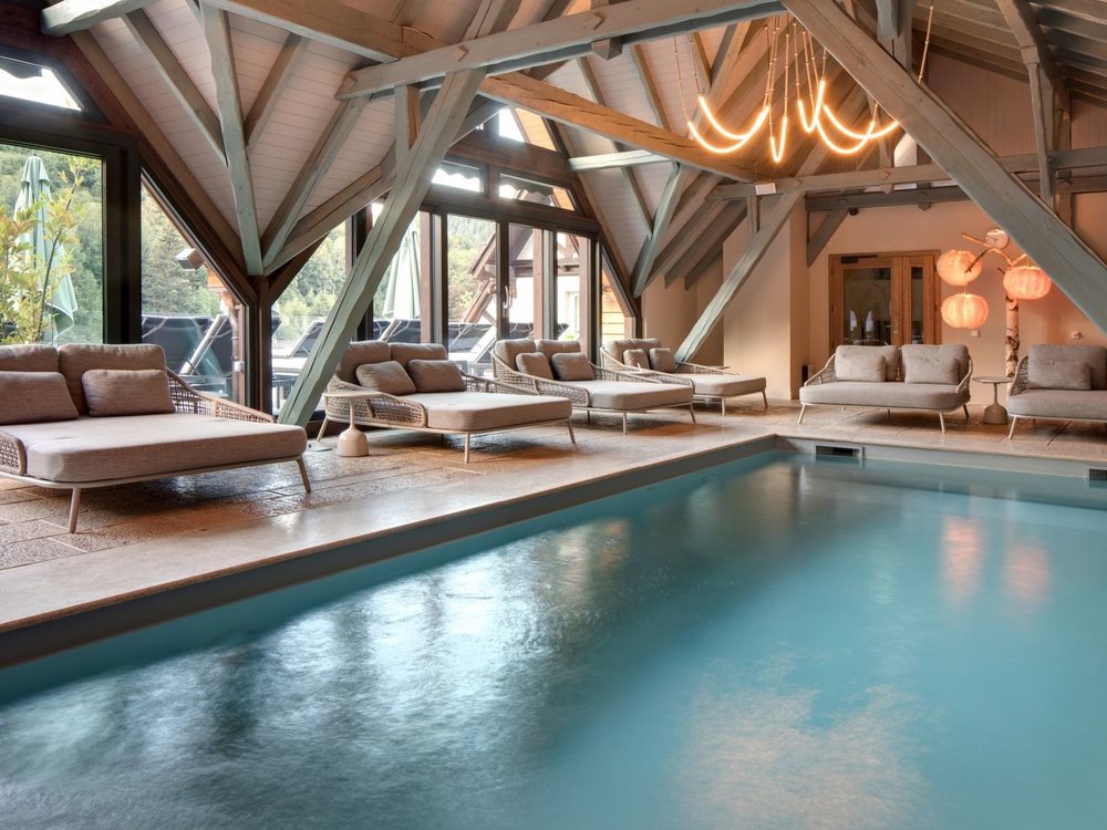 La piscine intérieure du Nature-Spa de La Cheneaudière sous sa charpente de bois, ses lits de repos et ses baies sur la forêt