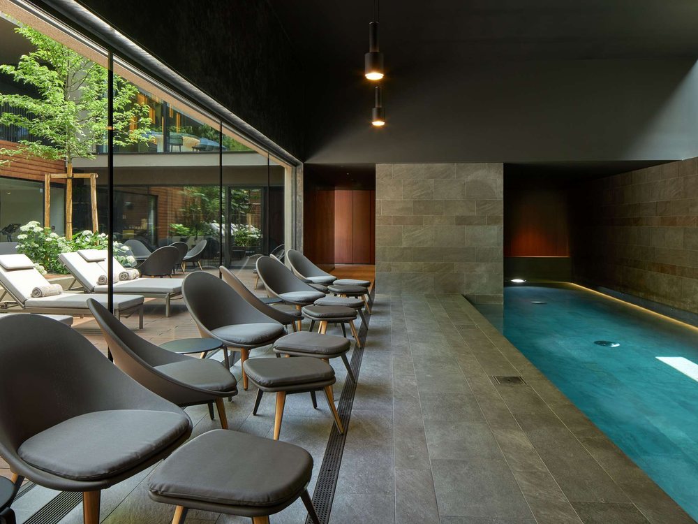 Le couloir de nage du spa de L'Esquisse à Colmar, ses fauteuils gris alignés et le patio planté derrière la baie vitrée