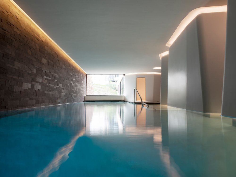 La piscine intérieure du spa des Haras à Strasbourg, son mur de pierre, sa lumière indirecte et la baie sur le jardin