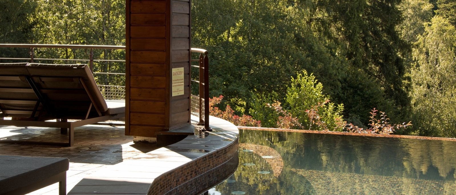 Le bassin extérieur à débordement du Nature-Spa de La Cheneaudière, un transat en bois et la forêt de la vallée de la Bruche