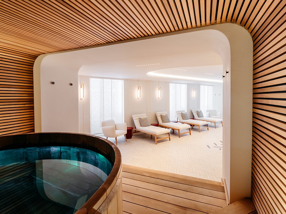 Le jacuzzi en forme de tonneau du Spa Maison Rouge, sous une arche en lattes de bois, et la salle de repos blanche derrière
