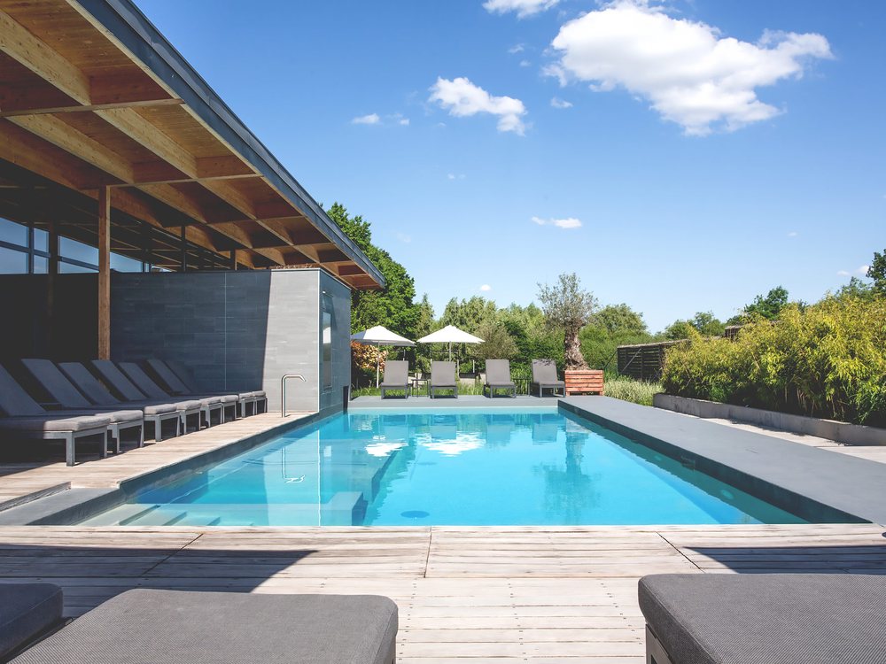 La piscine extérieure de La Source des Sens, ses transats gris sous l'auvent et le jardin arboré