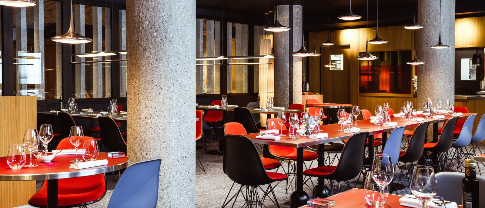 Une salle de restaurant de l'Altapura, ses piliers de béton, ses chaises colorées et ses tables dressées
