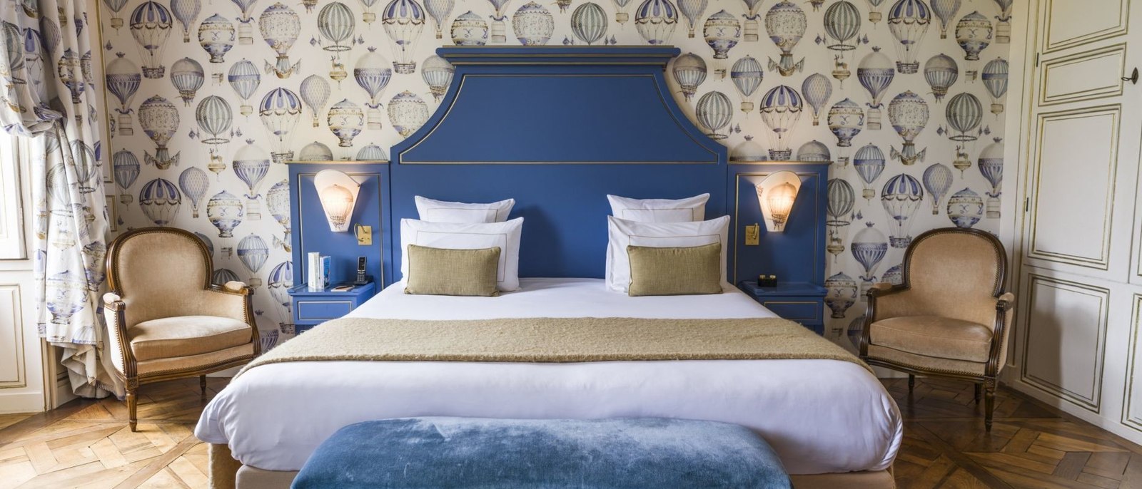 Une chambre du Château d'Audrieu, papier peint à montgolfières, tête de lit bleue, fauteuils Louis XVI et parquet en point de Hongrie