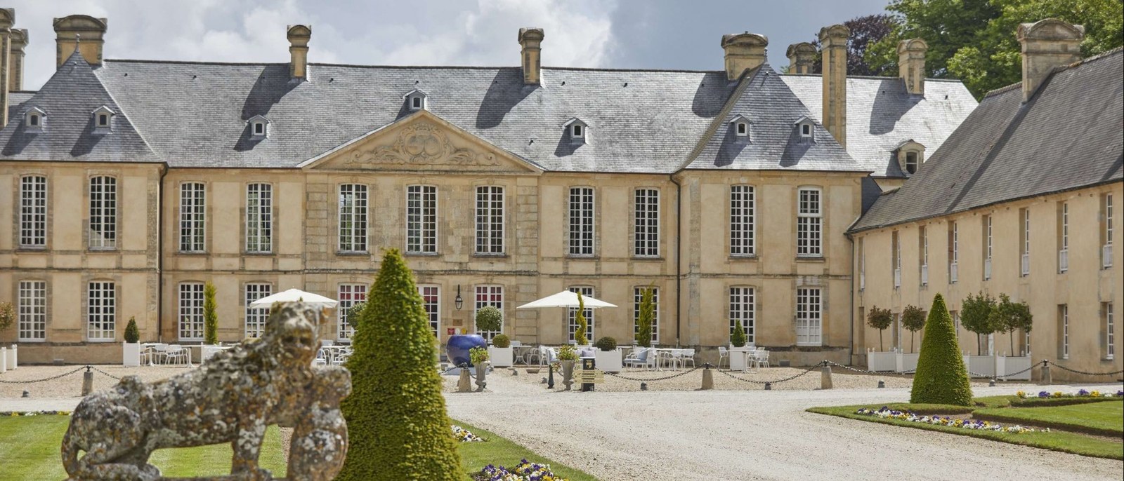 La façade du Château d'Audrieu, hôtel 5 étoiles du XVIIIe siècle dans le Calvados, toitures d'ardoise, fronton sculpté et cour de gravier bordée de buis