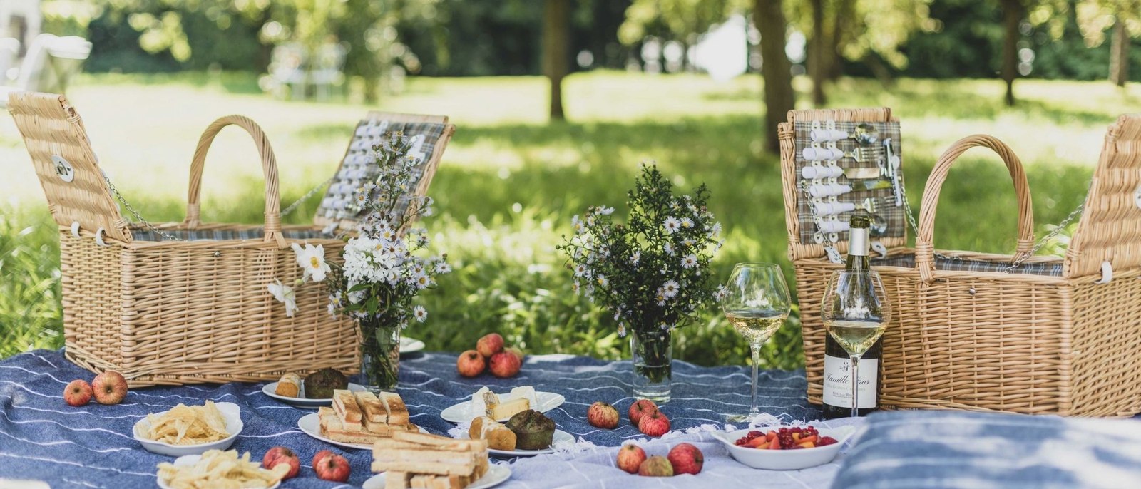 Un déjeuner dressé dans le parc du Château d'Audrieu, paniers d'osier, nappe bleue, pommes et bouquets de marguerites sous les arbres