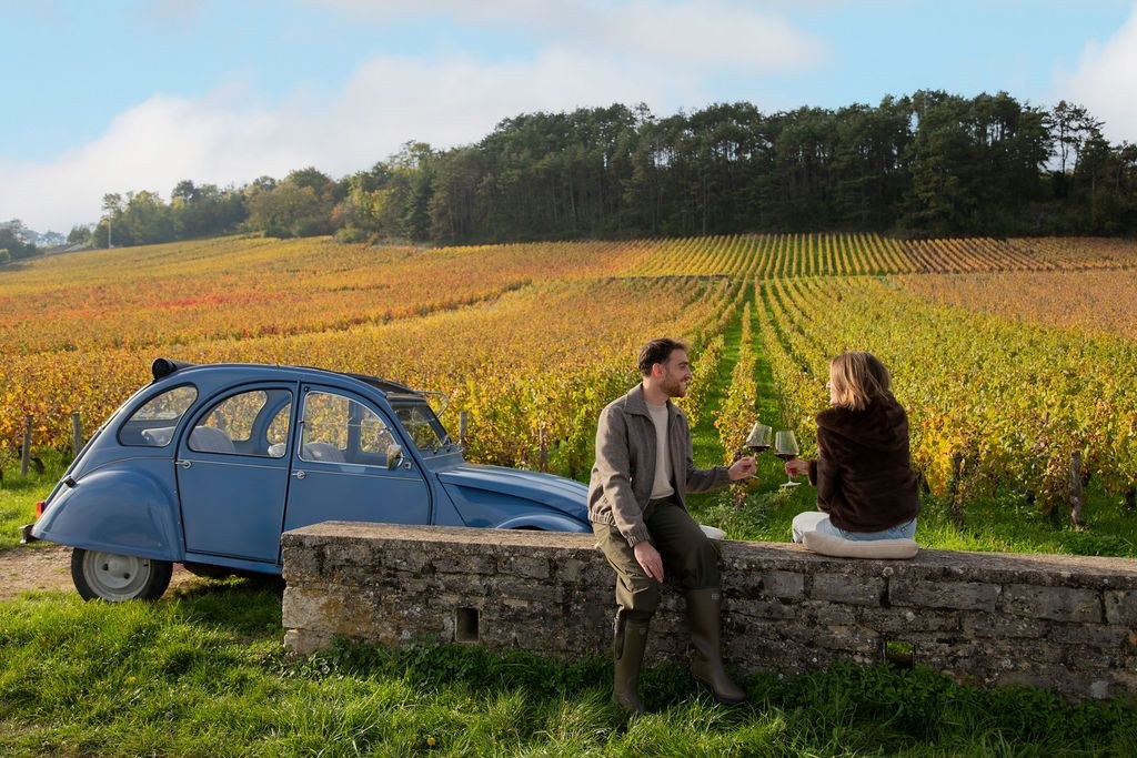 Une 2CV bleue et un couple dégustant un verre au bord des vignes de Pommard en automne