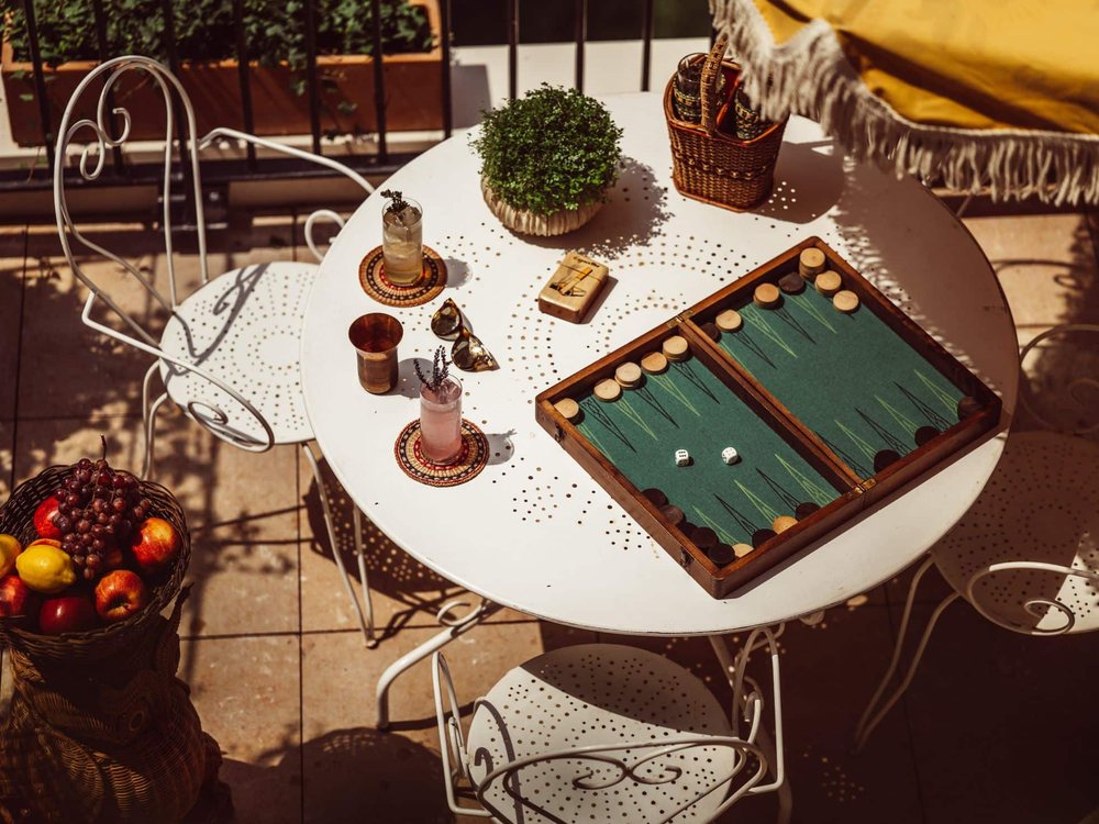 Une table de jardin de Monsieur Aristide, son backgammon, ses fruits et ses chaises de fer blanches au soleil