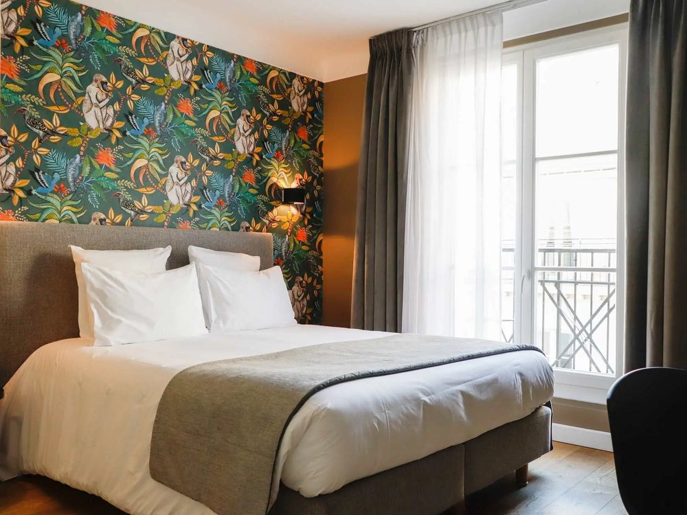 Une chambre de l'Hôtel Mathis, son papier peint tropical, son lit blanc et sa porte-fenêtre sur balcon