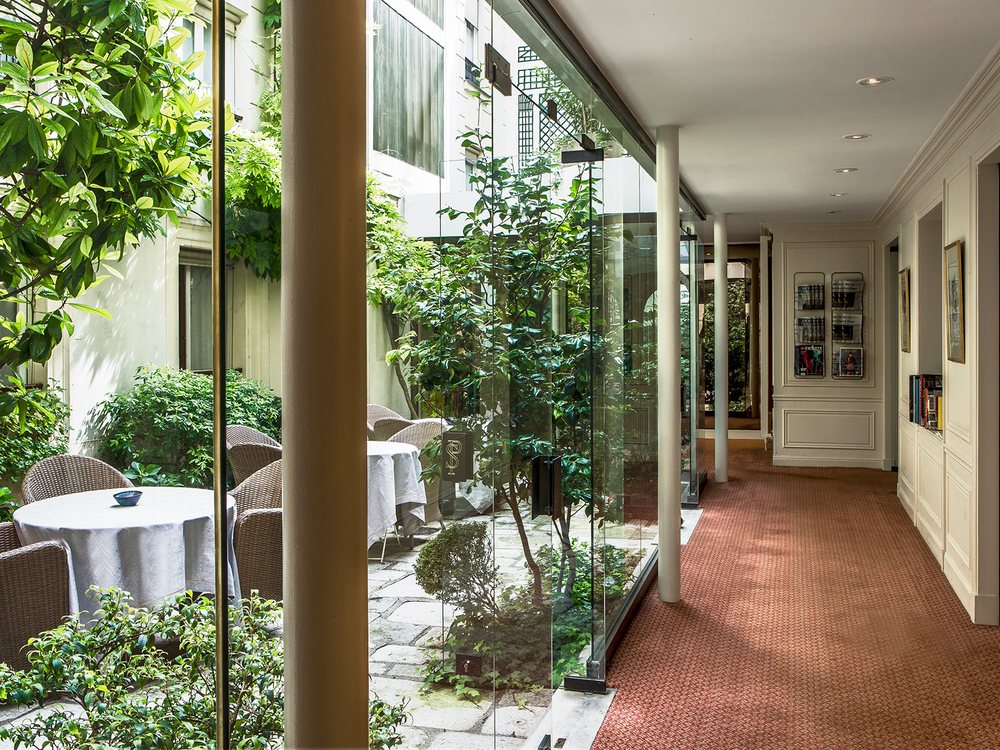 La galerie vitrée de l'Hôtel des Saints-Pères, ouverte sur un patio arboré aux tables de jardin