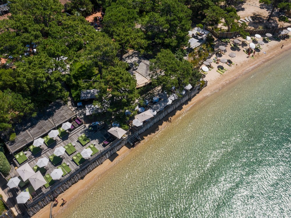 La plage du Grand Hôtel de Cala Rossa vue du ciel, ses transats sous la pinède et l'eau turquoise de la baie