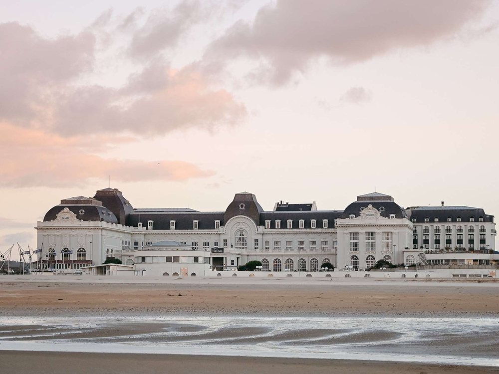 Les Cures Marines vues depuis la plage de Trouville à marée basse, leur longue façade blanche sous un ciel rose