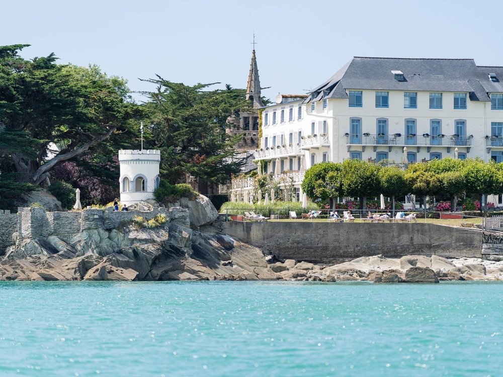 Le Grand Hôtel des Bains de Locquirec vu de la mer, sa façade blanche au-dessus des rochers et de l'eau claire