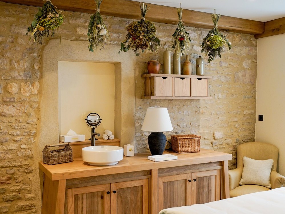 Une cabine du Spa Sisley de l'Hostellerie de Levernois, murs de pierre sèche et bouquets de fleurs séchées suspendus