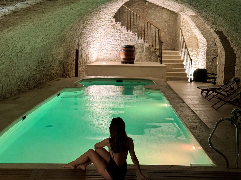 La piscine intérieure du Château de Vault-de-Lugny, bassin vert d'eau sous une voûte de pierre et tonneau de vin