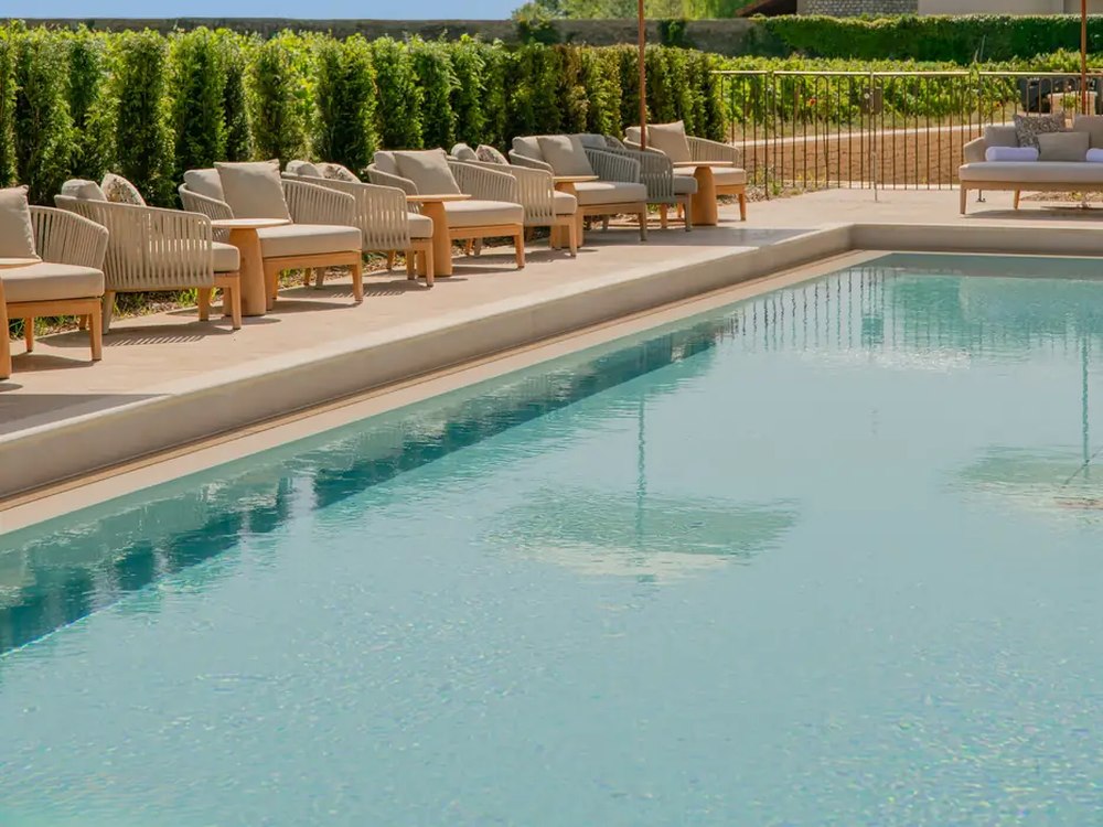 La piscine extérieure chauffée du Château la Commaraine, bains de soleil en rotin et haie taillée devant les vignes de Pommard