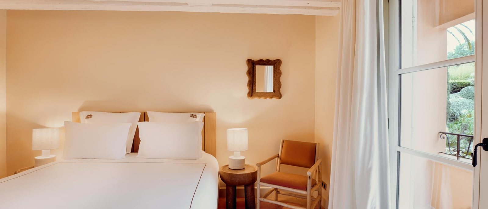 Une chambre de La Bastide de Saint-Tropez, ses murs clairs, son sol de tomettes et sa porte-fenêtre ouverte sur le jardin