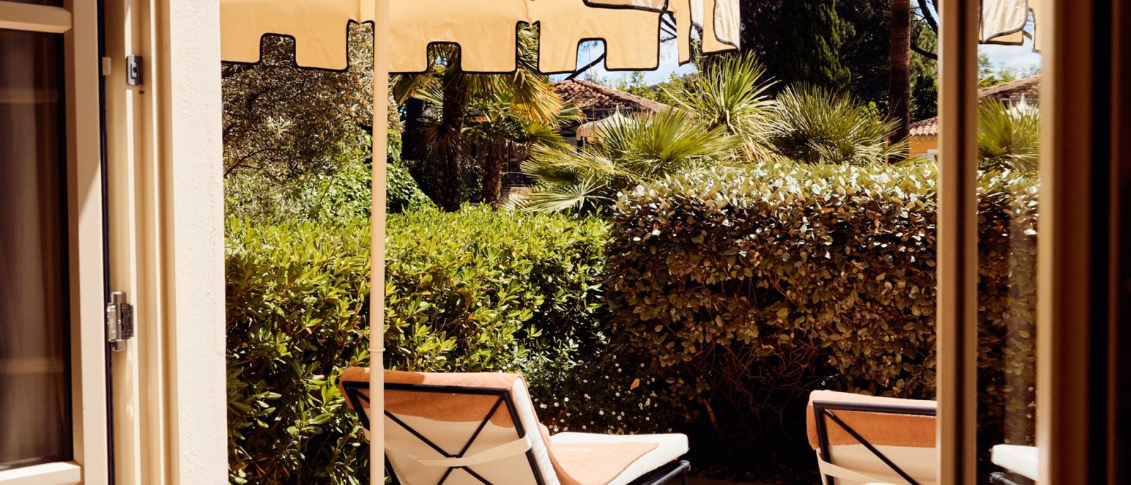 La terrasse d'une chambre de La Bastide de Saint-Tropez, ses transats sous un parasol à franges, face au jardin et aux palmiers