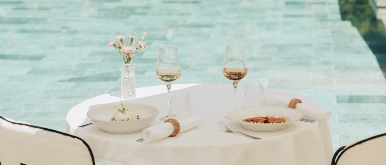 Une table dressée au bord de la piscine de La Bastide de Saint-Tropez, verres de vin rosé, fleurs et assiettes, devant l'eau turquoise
