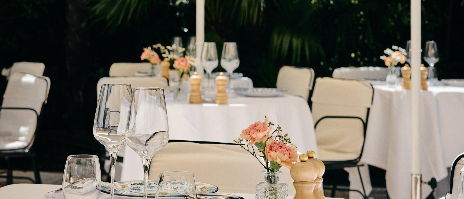 Les tables de La Trattoria de La Bastide de Saint-Tropez, nappes blanches, fleurs roses et chaises de rotin, sous les palmiers