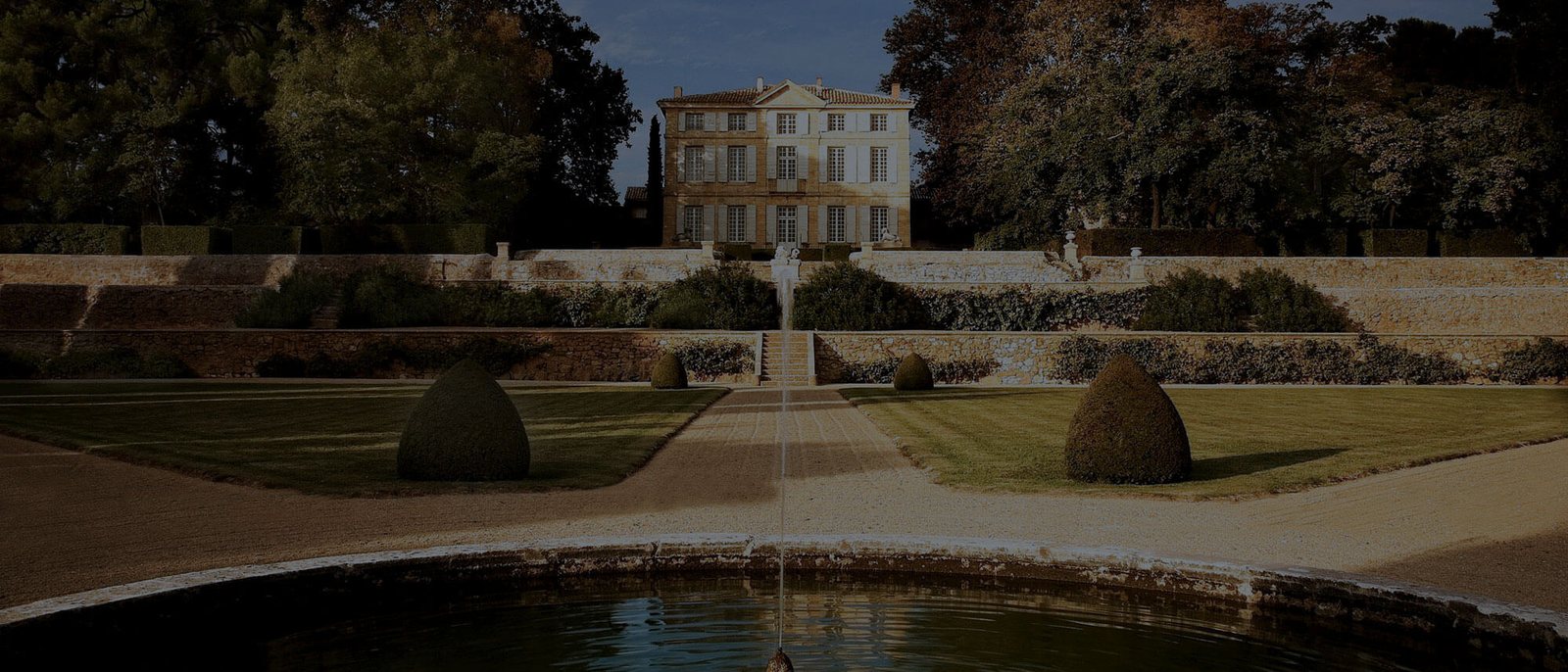 La façade de la bastide du Château de la Gaude au crépuscule, derrière son jardin et son bassin