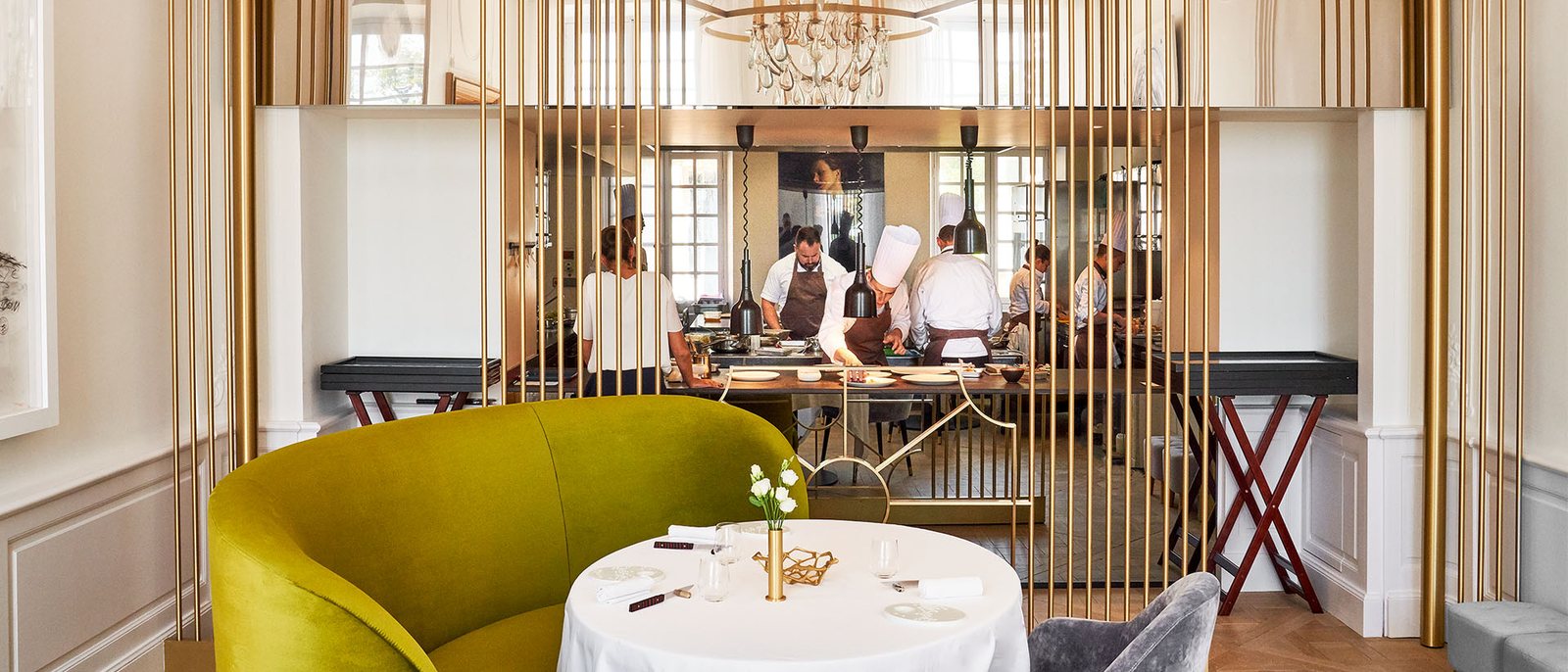 La salle du restaurant Le Art, ses fauteuils jaunes, sa table dressée et la cuisine ouverte derrière une claustra dorée