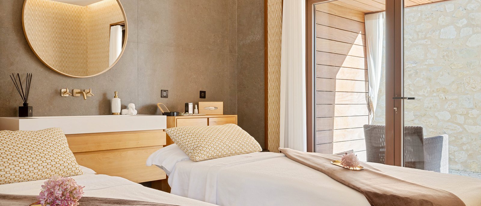 Une cabine de soins en duo du spa du Château de la Gaude, deux tables de massage, un miroir rond et une baie sur la pierre