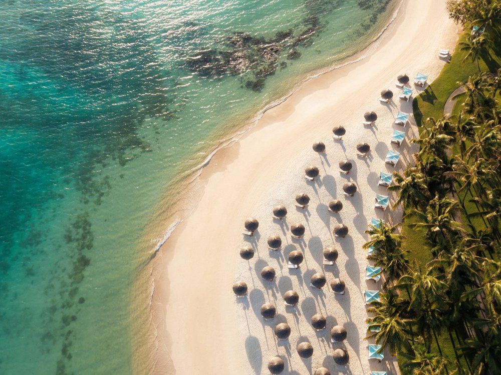Vue aérienne de la plage du One&Only Le Saint Géran, ses parasols de chaume et son lagon