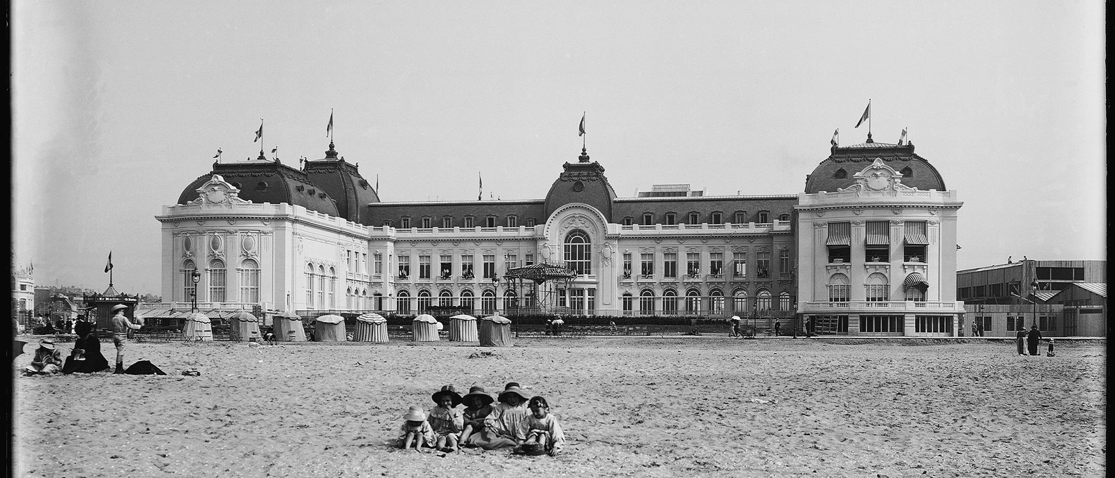 Le casino de Trouville-sur-Mer au début du XXe siècle, photographie ancienne en noir et blanc prise depuis la plage, des enfants assis sur le sable