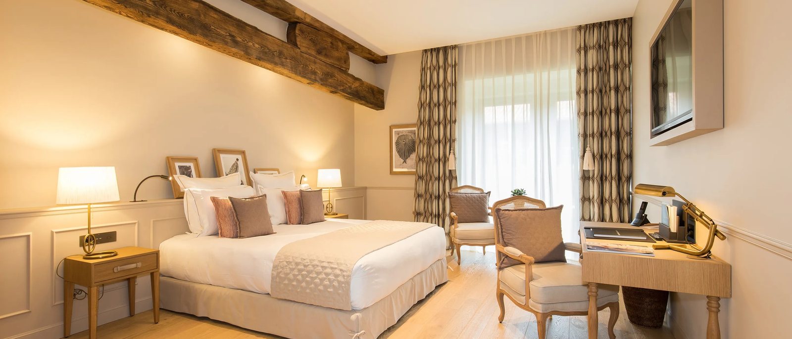 Une chambre de l'Hôtel Chais Monnet, ses tons crème, sa poutre ancienne et ses rideaux ouverts sur la terrasse