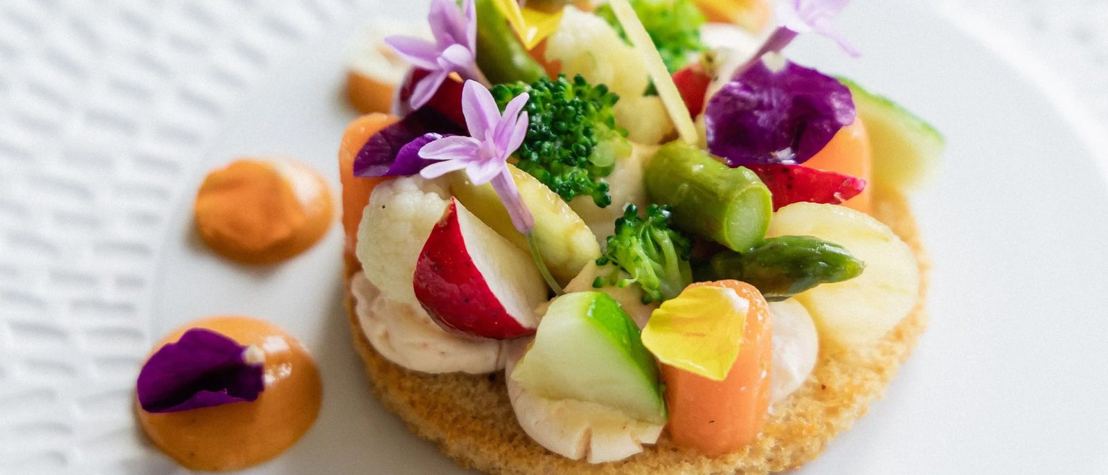 Une assiette de légumes croquants et de fleurs comestibles sur une tartelette, dressée sur une assiette ciselée