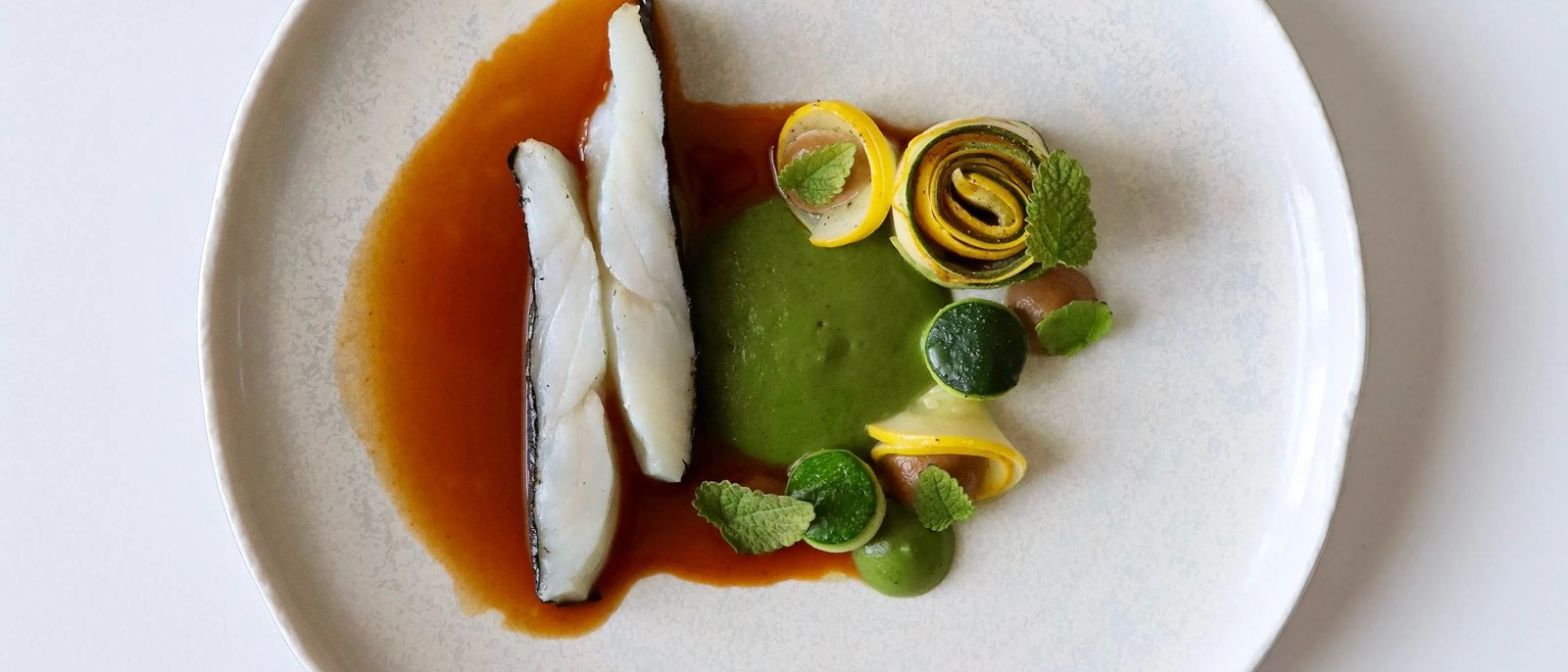 Une assiette des Foudres, poisson et sauce ambrée, légumes verts roulés, sur une assiette blanche