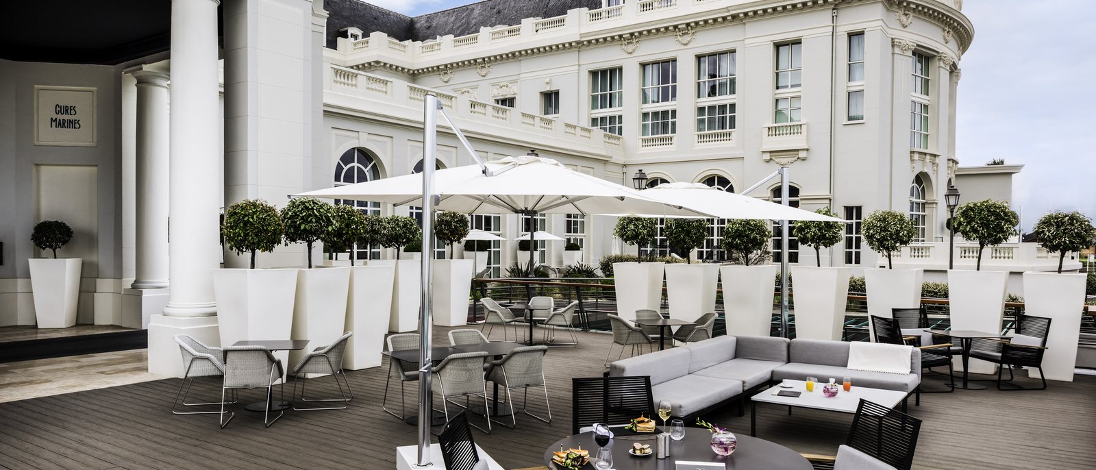 La terrasse des Cures Marines au pied de la façade blanche, ses parasols, ses canapés et ses orangers en pot