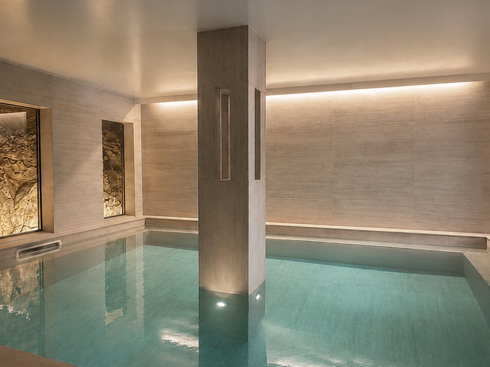Le bassin intérieur chauffé du spa Casamore, ses murs de pierre claire, son pilier central et son éclairage indirect