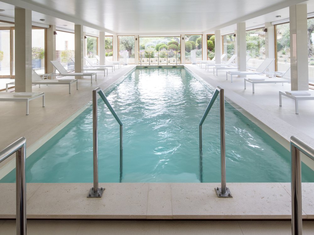 La piscine intérieure chauffée de La Villa à Calvi, ses colonnes blanches, ses transats et les baies ouvertes sur le jardin