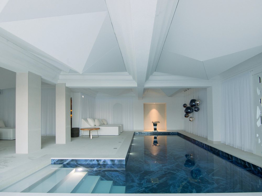La piscine intérieure chauffée du Spa by Clarins de l'Hôtel Marinca, son bassin bleu nuit, ses murs blancs et ses sphères suspendues