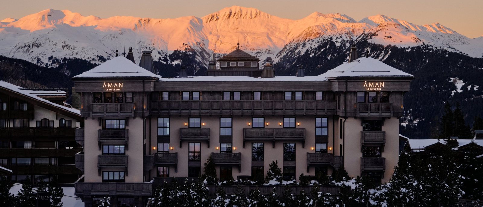 Aman Le Mélézin au coucher du soleil, sa façade de château au-dessus de Courchevel 1850 et les sommets roses derrière