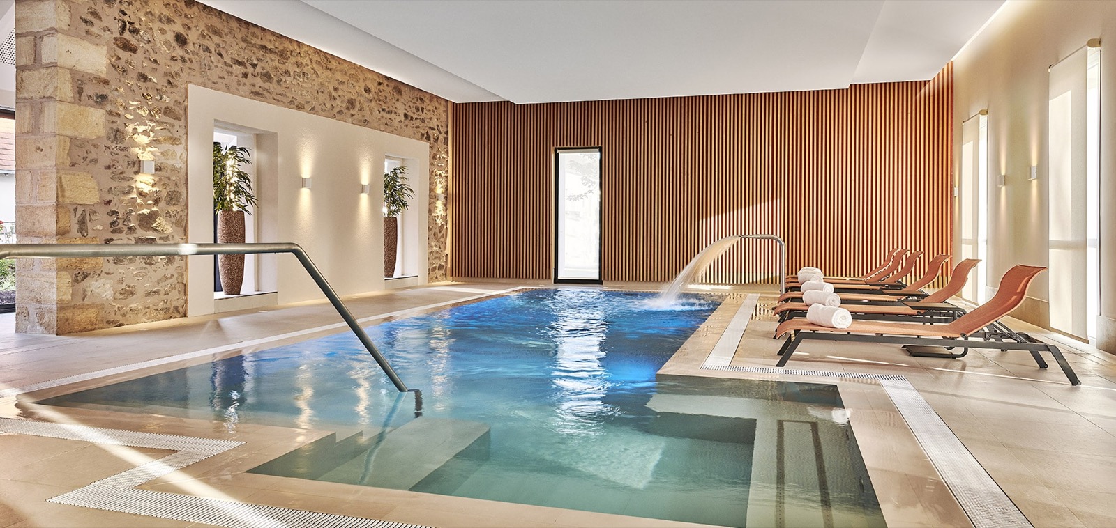 La piscine intérieure du spa du Château Saint-Jean, jacuzzi intégré, mur de pierre et claustra de bois
