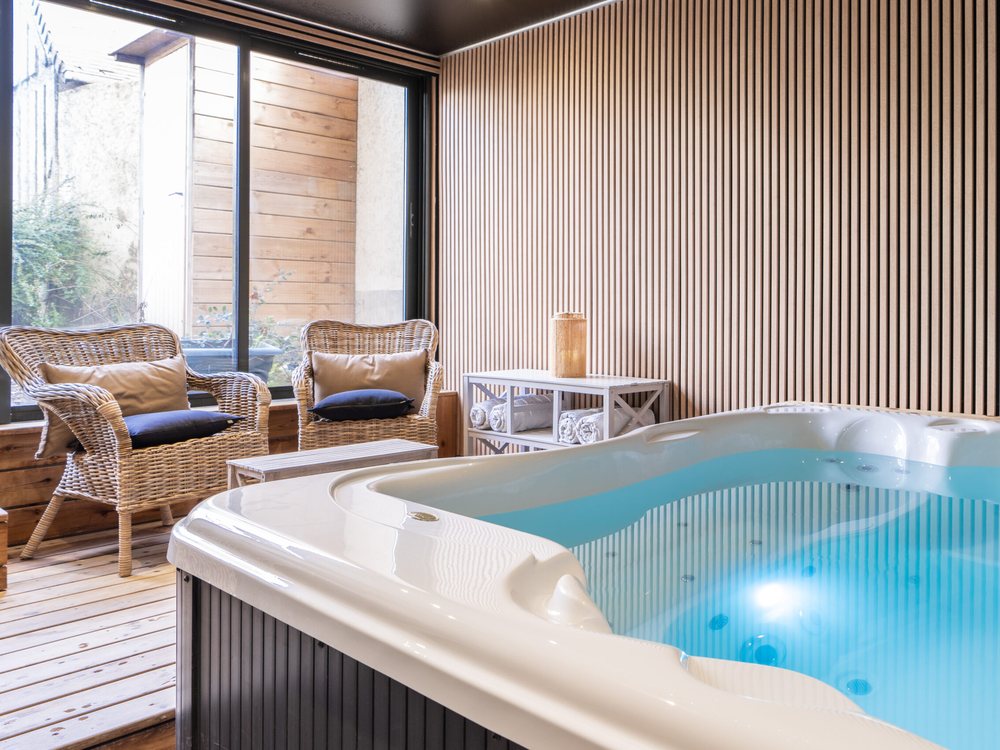 Le jacuzzi de l'Augeval Spa, à la Villa Augeval, devant des fauteuils en rotin et une baie ouverte sur une terrasse