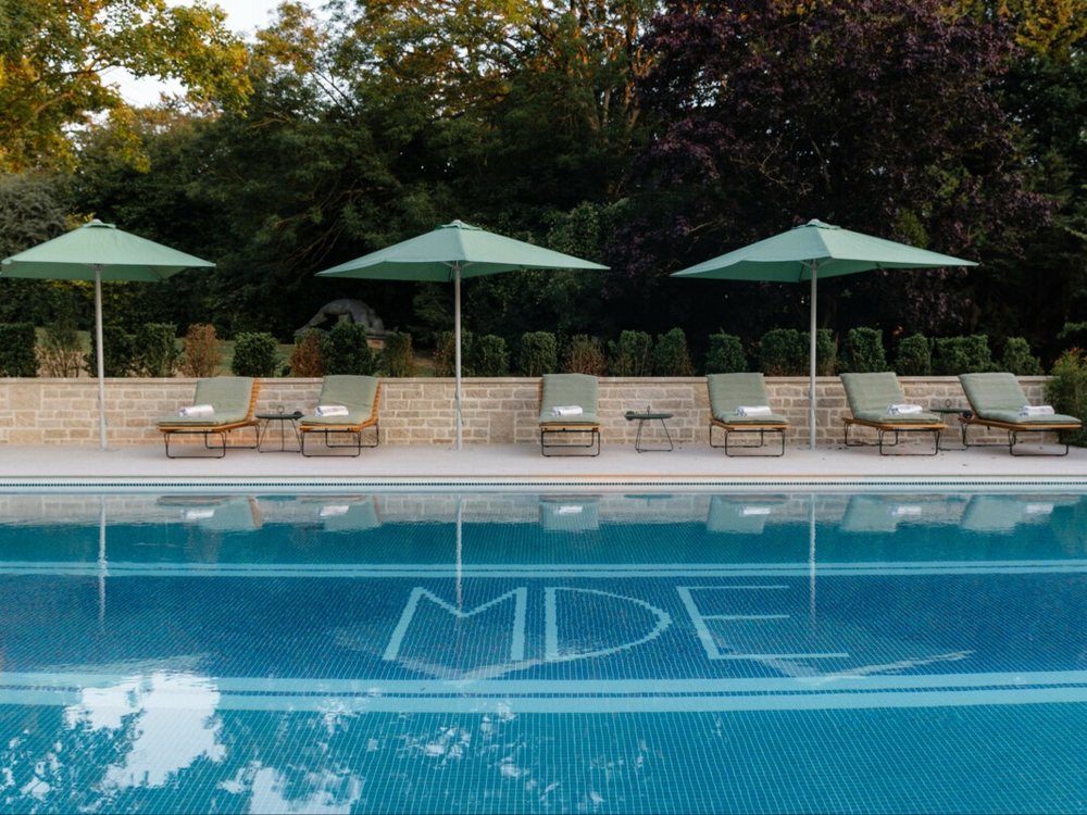 La piscine extérieure de Maison Douce Époque, ses transats et ses parasols verts, ses initiales en mosaïque au fond du bassin