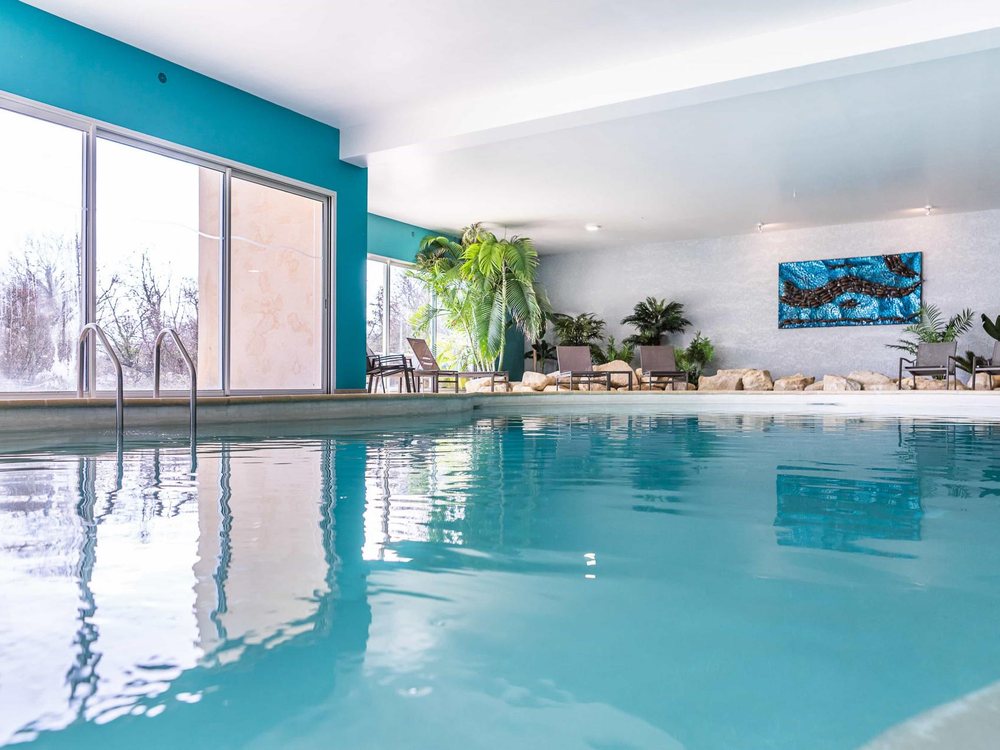 La piscine intérieure du Domaine de Villers, tout en courbes, sous de grandes baies vitrées ouvertes sur le jardin